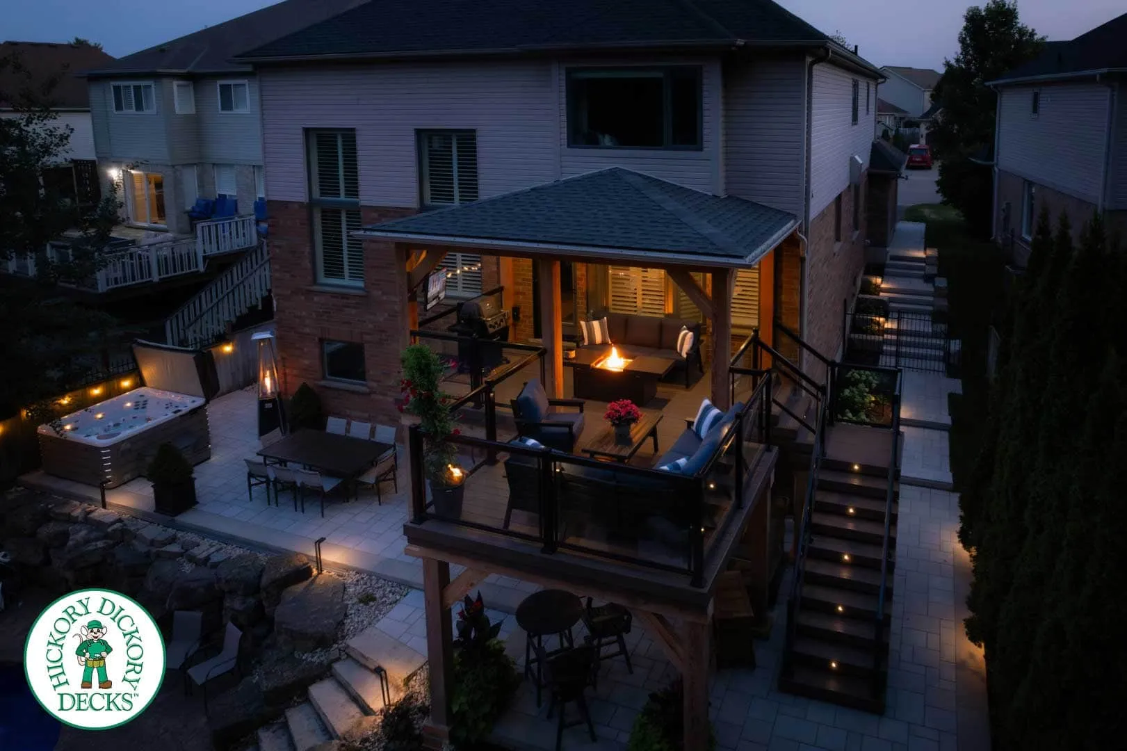 HDD_CustomRoof_Watermarked Two-story deck and patio illuminated at night.