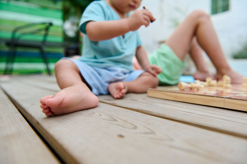 Children playing chess outdoors on a wooden deck during a sunny afternoon